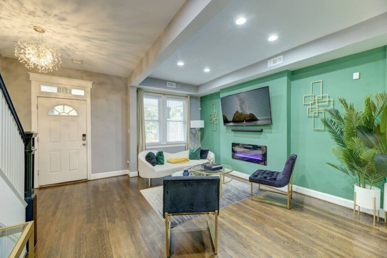 A living room with a white sofa, a black armchair, a coffee table, and a TV mounted on the wall.