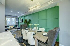 A dining area with a table set for four, surrounded by chairs, in a room with green paneled walls and a modern chandelier. - Spacious 4BR DC Home | 2 Parking Spots | Sleeps 8 (Washington)