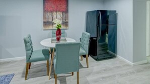 Un comedor con una mesa redonda, cuatro sillas, un florero con flores y un cuadro en la pared.