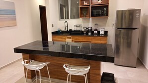 A modern kitchen with a central island, wooden cabinets, a stainless steel refrigerator, and two white bar stools. - 3. Vista al mar turquesa. (Progreso)