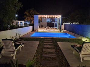 Un jardin avec une piscine, une terrasse en bois et du mobilier d’extérieur.