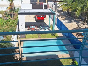 Une piscine avec un patio couvert, un camion rouge garé à proximité et des palmiers en arrière-plan.