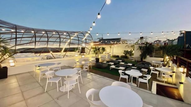 An outdoor seating area with round tables and chairs, string lights, and a covered seating area with cushions. - Aurora Suites Pasay near Airport (Pasay)