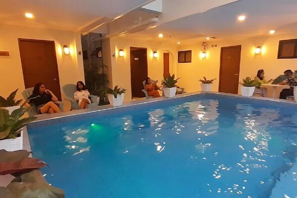An indoor swimming pool with a clear blue water surface, surrounded by seating areas with potted plants. - Aurora Suites Pasay near Airport (Pasay)