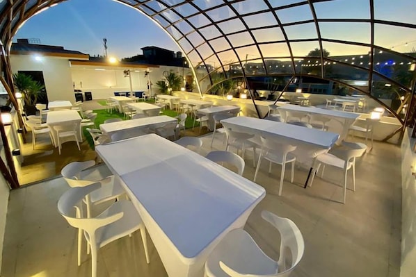 Een terras met witte tafels en stoelen, overdekt met een glazen constructie.