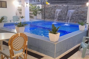 A pool with a waterfall feature, surrounded by chairs and potted plants. - Aurora Suites Pasay near Airport (Pasay)