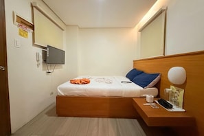 A small, modern bedroom with a single bed, a bedside table, a mounted TV, and a wall-mounted light. - Aurora Suites Pasay near Airport (Pasay)