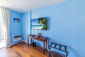 A room with a wooden desk, a chair, a mounted TV, and a window with curtains.