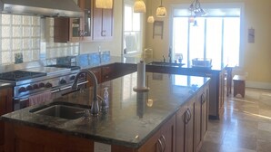 Un'ampia cucina con un'isola grande, elettrodomestici in acciaio inossidabile, luci a sospensione e vista sull'area pranzo.
