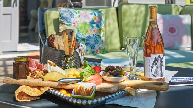 Een tafel gedekt met diverse gerechten en een fles wijn, met een huis en een raam op de achtergrond.