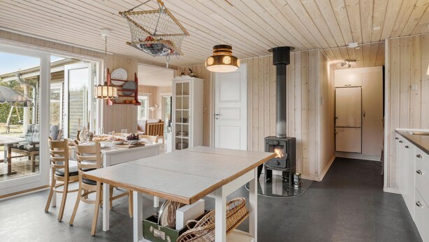 A modern kitchen with a central island, a wood-burning stove, and a dining area with a table and chairs. - 2 bedroom beautiful home in Hals (Hals)