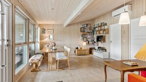 A cozy, well-lit room with wooden floors and walls, a dining area with a table and chairs, a bookshelf filled with books, and a television. - 2 bedroom beautiful home in Hals (Hals)