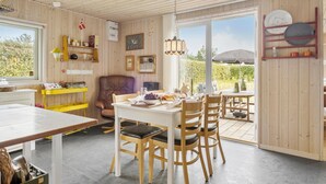 A cozy dining area with a table set for four, surrounded by wooden chairs. A brown leather chair is placed near the window, and a yellow shelf holds various items. - 2 bedroom beautiful home in Hals (Hals)