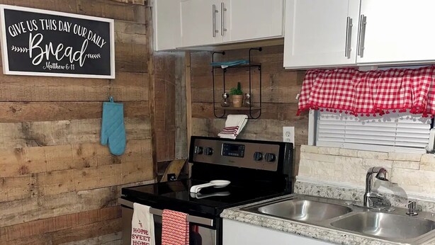 Una cocina con armarios blancos, una estufa de acero inoxidable y una encimera de granito. Hay un cartel en la pared y un mantel individual en el suelo.