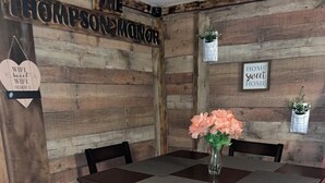 Un comedor rústico de madera con una mesa y sillas, un letrero que dice “THE THOMPSON MANOR” y un cartel que reza “HOME sweet HOME”.