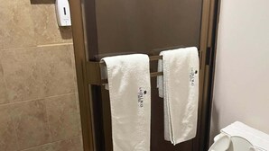 Un baño con ducha envuelta en vidrio, un inodoro y dos toallas blancas colgadas en un perchero.