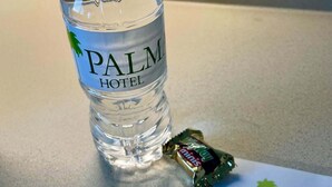 Una botella de agua con la etiqueta "PALM HOTEL" y una pequeña barra de chocolate sobre una mesa con una tarjeta de bienvenida.