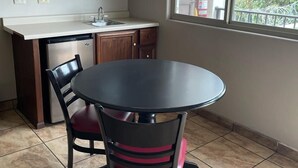 Cocina compacta con una mesa redonda para comer, dos sillas, microondas y ventana con vista a vegetación.