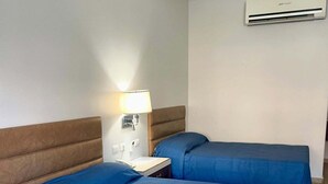 Una habitación de hotel con dos camas, una mesita de noche, una lámpara y un equipo de aire acondicionado.