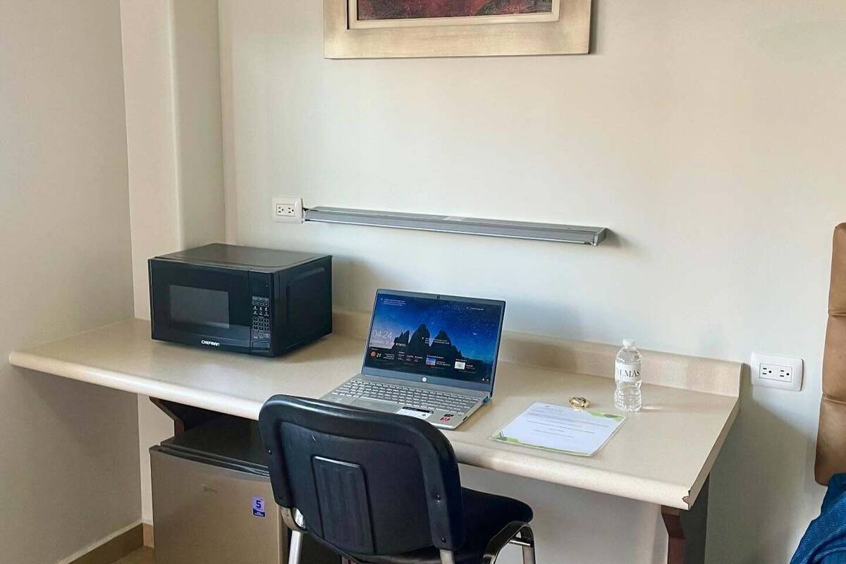 A compact office space with a desk, a laptop, a microwave, and a refrigerator.