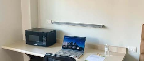 Un espacio de oficina compacto con escritorio, laptop, microondas y refrigerador.