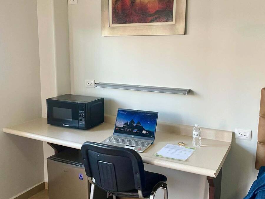 Un espacio de oficina compacto con escritorio, laptop, microondas y refrigerador.