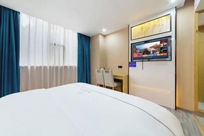 Hotellihuone, jossa on sänky, työpöytä, tuoli, seinälle asennettu televisio ja ikkuna, jossa on verhot.
