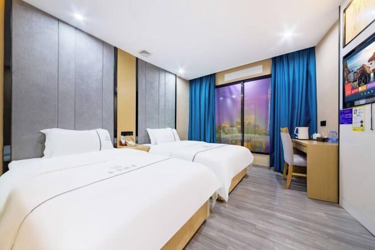 Habitación de hotel con dos camas, un escritorio, una silla y un ventanal con cortinas.
