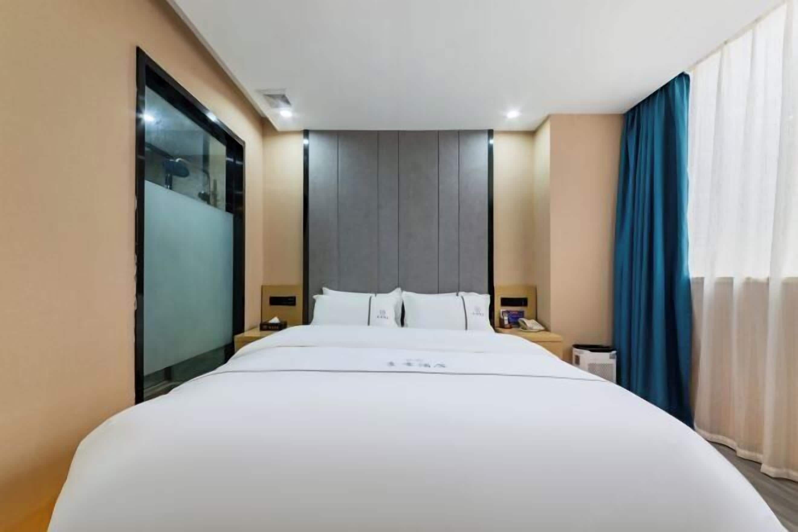 Ein Hotelzimmer mit einem großen Bett, einem Kopfteil, Nachttischen und einem Fenster mit Vorhängen.