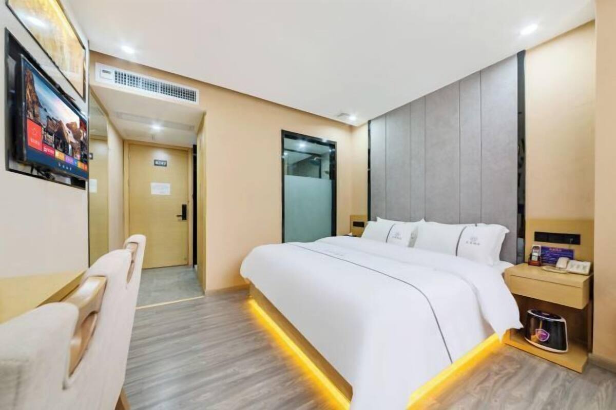 Una habitación de hotel con una cama, mesita de noche y televisión en la pared.