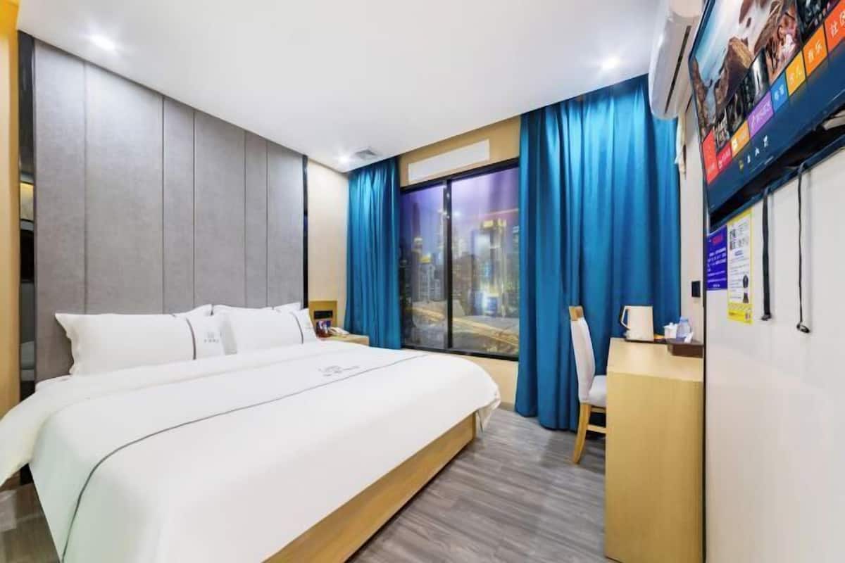 Una habitación de hotel con cama, escritorio, silla, ventana con cortinas y televisor montado en la pared.