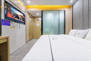 Hotellihuone, jossa on sänky, seinälle asennettu televisio, puinen työpöytä ja ovi, jossa on numerokyltti.