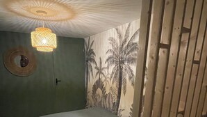 Une chambre avec un lit, un luminaire suspendu, un miroir mural et un papier peint à motifs tropicaux.