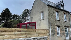 Un bâtiment en pierre avec un toit en pente, une cheminée et une fenêtre à cadre rouge.