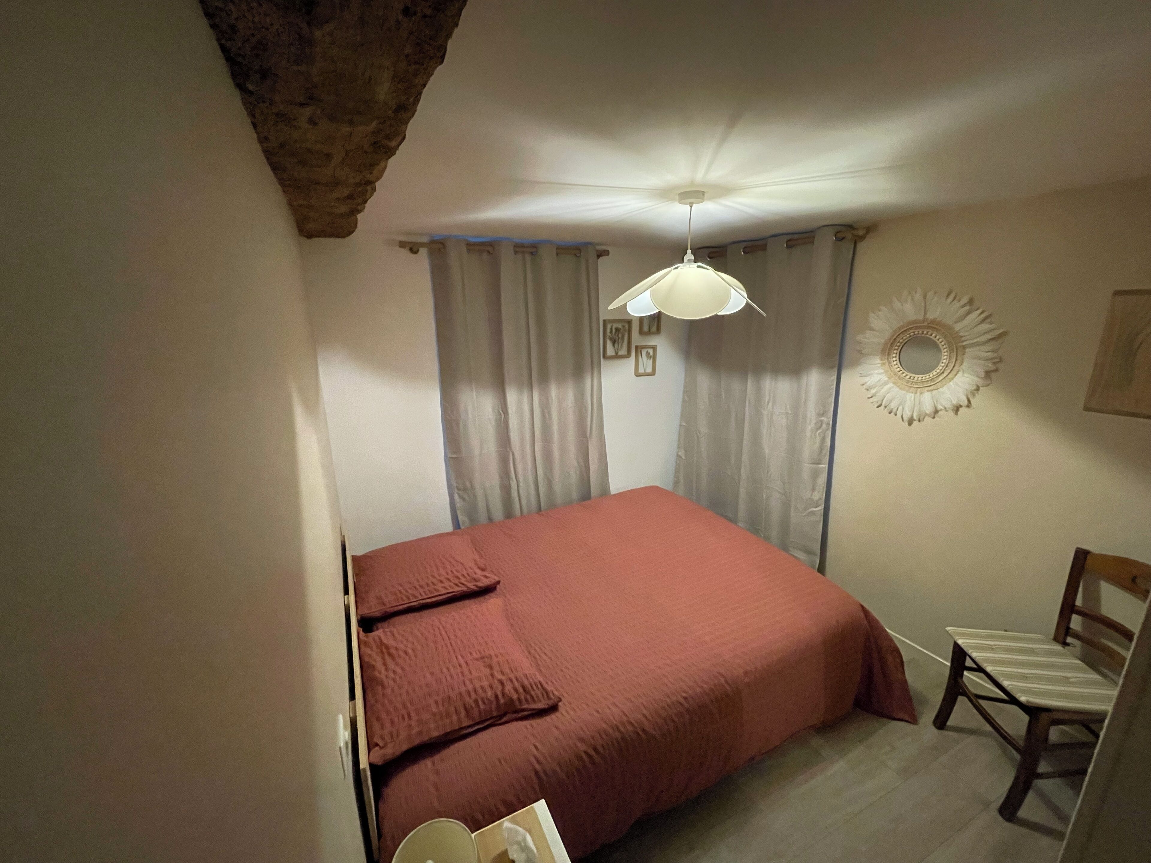 Un dormitorio con cama, una silla, ventilador de techo y espejo adosado a la pared.