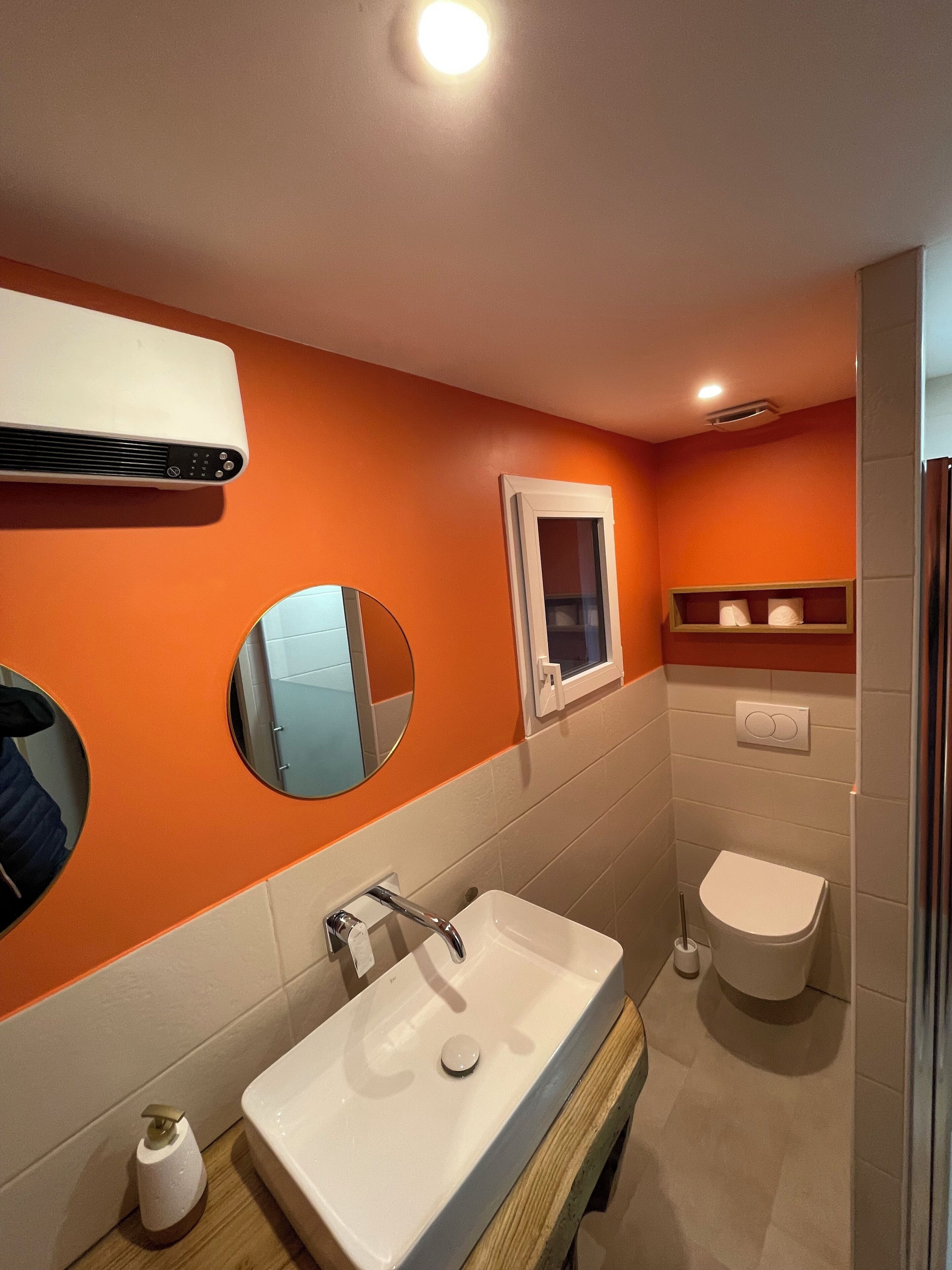 Un bagno con una parete arancione, un lavandino bianco, uno specchio, una finestra e un water.