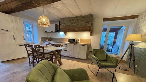 Une cuisine moderne avec des meubles blancs, une table à manger et des chaises. On y trouve également un canapé vert et un lampadaire.