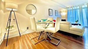 Een moderne woonkamer met een eettafel, witte stoelen, een vloerlamp en een bank.