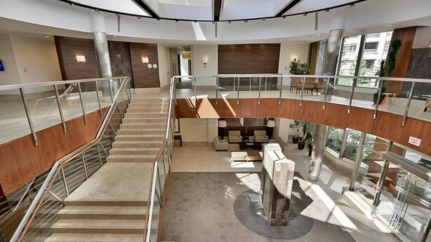 Een modern interieur met een centrale trap, een zithoek en een glazen balustrade.