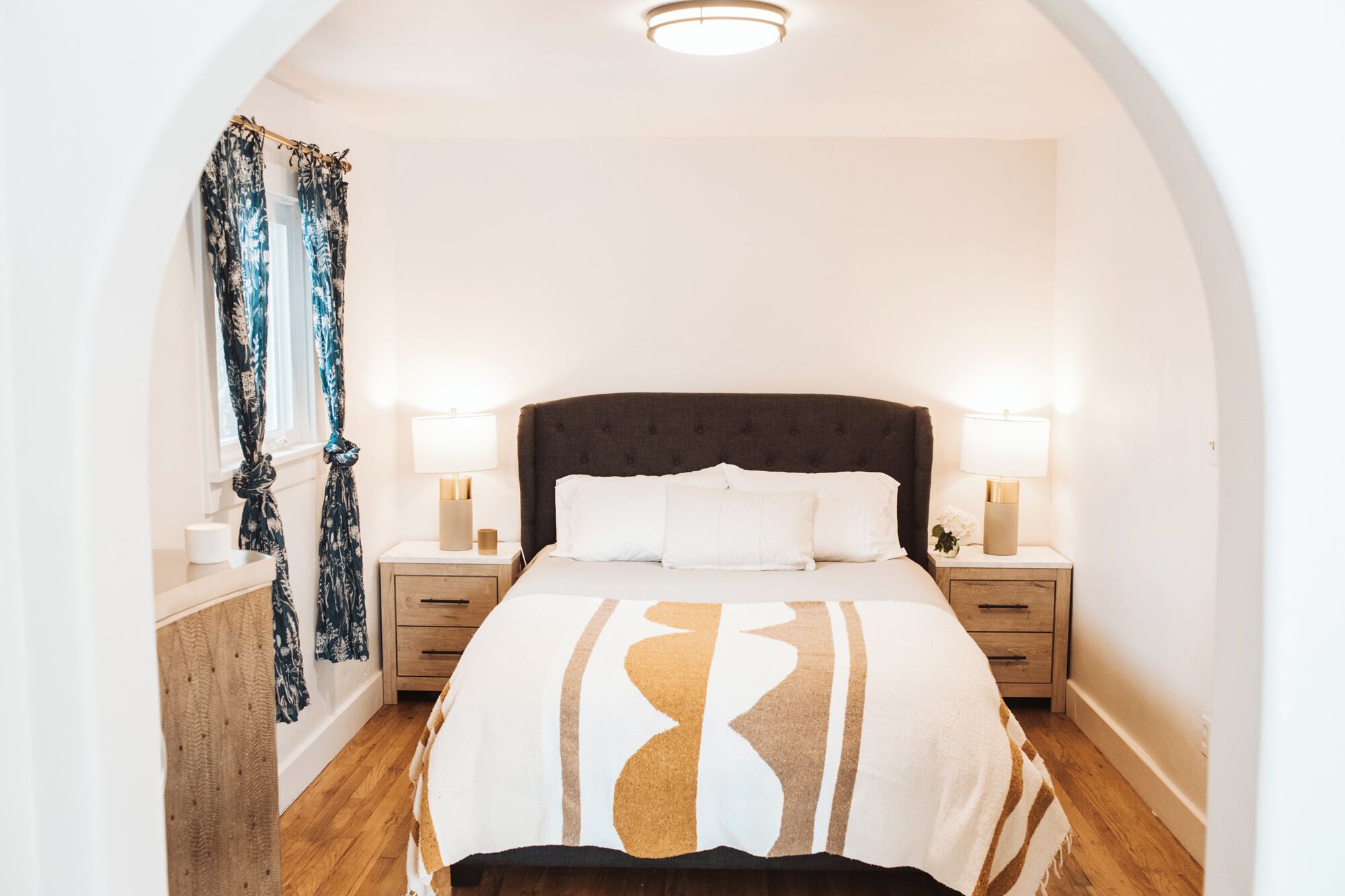 A bedroom with a large bed, two bedside tables, a window with curtains, and a ceiling light.