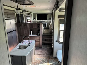Eine kompakte Küchenzeile für Wohnmobile mit einem Edelstahlkühlschrank, einer Spüle, einer Kaffeemaschine und einer kleinen Essecke.