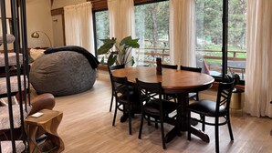 Un coin repas accueillant avec une table et des chaises en bois, un grand fauteuil en forme de poire et une vue sur l’extérieur grâce à de grandes fenêtres.