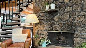 Une cheminée en pierre avec un paravent en métal, un fauteuil en cuir marron avec un coussin blanc et une lampe.