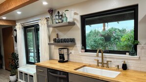 Une cuisine moderne dotée d’un plan de travail en bois, d’un évier encastré et d’une fenêtre donnant sur un paysage verdoyant.