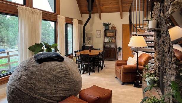 Un vaste espace de vie doté d’un haut plafond, de poutres en bois, d’un grand pouf rond, d’un canapé en cuir marron et d’un mur en pierre agrémenté de plantes.