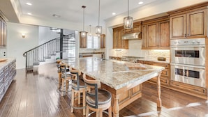 A spacious kitchen with a large island, wooden cabinets, stainless steel appliances, and a modern staircase. - The Castle-Pool/Spa/Billiard (Henderson)