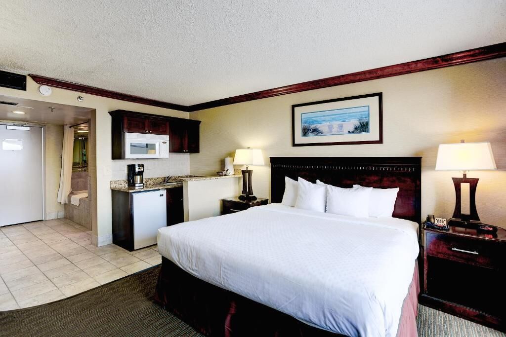Een hotelkamer met een groot bed, een kleine kitchenette, een badkamer en een inlijsting foto aan de muur.