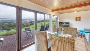 A spacious balcony with wicker furniture, a table set for dining, and a scenic view of the countryside.