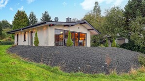 A modern house with a large glass window, a stone wall, and a grassy area.