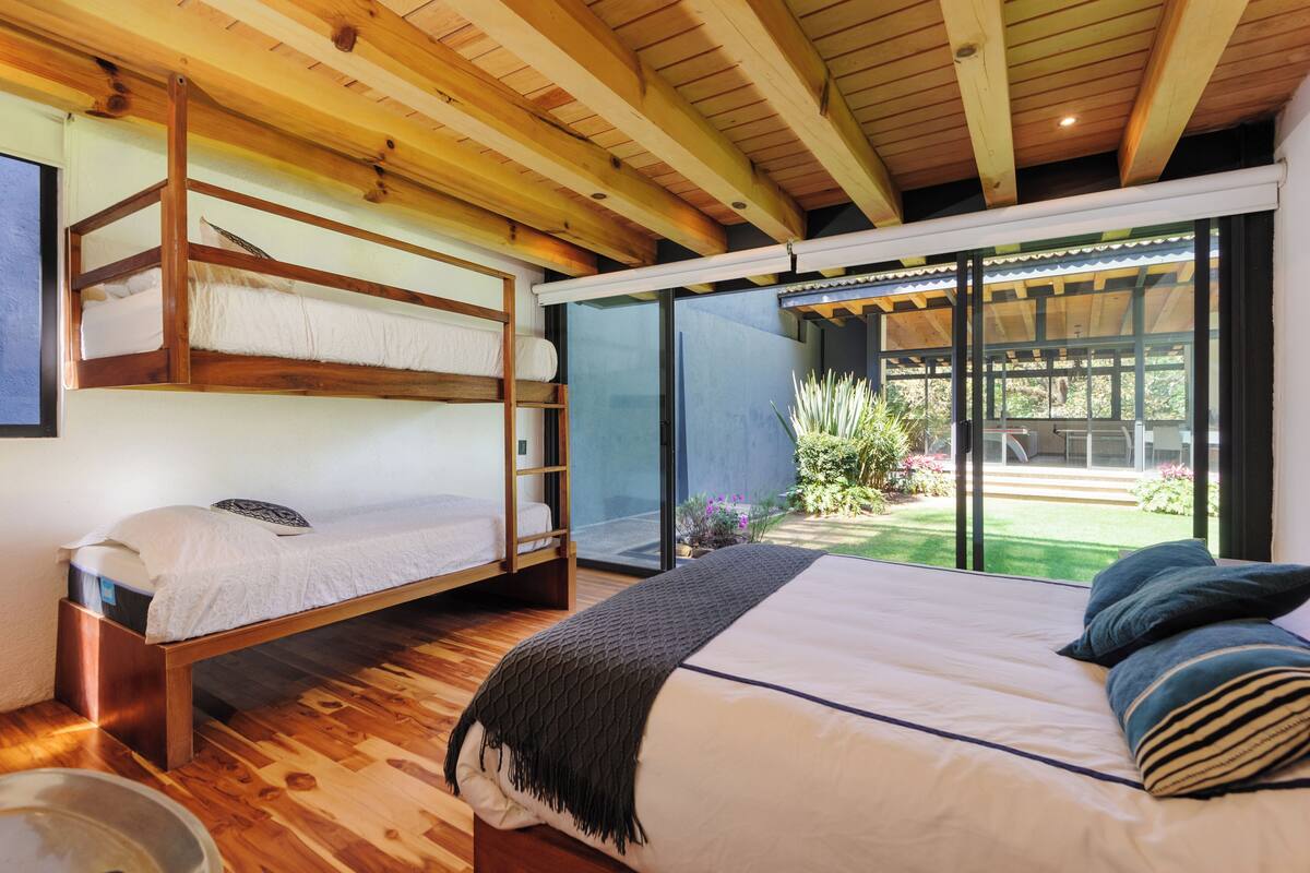 A bedroom with a bunk bed, a single bed, and a large sliding glass door leading to a garden.